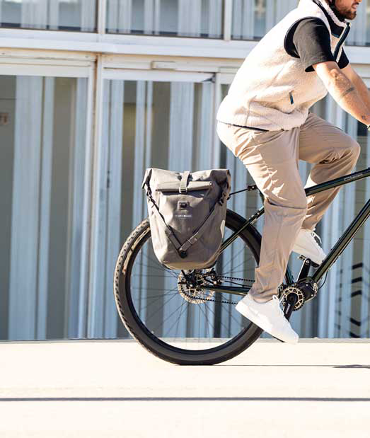 Ortlieb Fahrradtasche in Aktion - beige gekleidete Person fährt auf Rad, an dessen Hinterrad Ortlieb Taschen montiert sind