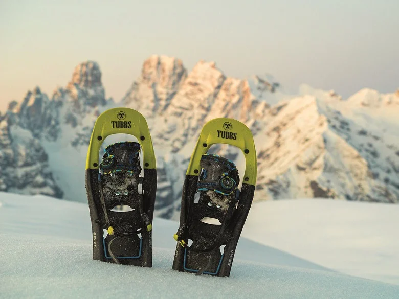 Outdoor Imagebild - zwei Schneeschuhe in schwarz mit grüner Spitze stecken im Schnee. Im Hintergrund Berge.
