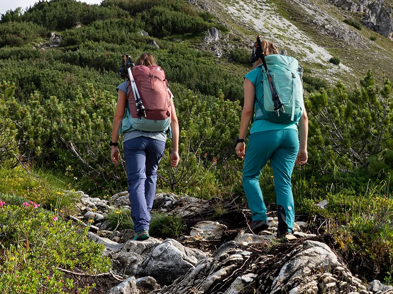 deuter Trail Rucksack Outdoor Imagebild - zwei Personen wandern im Gebirge mit Wanderrucksack, außen am Rucksack ist je ein Paar Wanderstöcke befestigt.