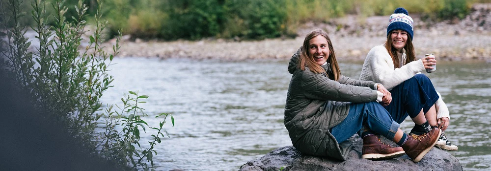 Outdoor Imagebild - zwei Personen sitzen auf einem Felsen, im Hintergrund fließt ein Fluss vorbei