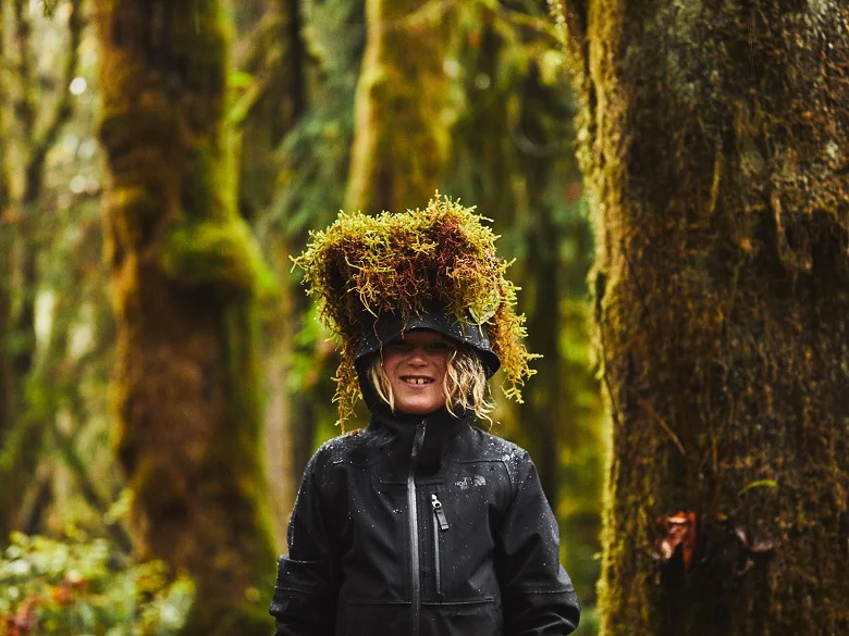Outdoor Imagebild - Person im Wald mit Regenjacken. An den Baumstämmen wächst Moos.