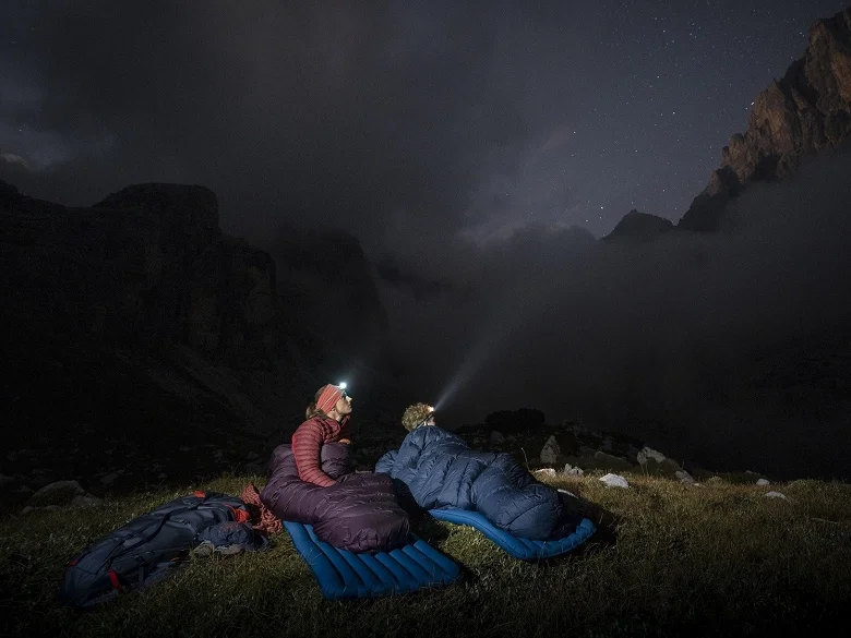 Warum ein Kunstfaserschlafsack? Outdoor Imagebild - zwei Personen übernachten im Freien auf Isomatten und in Outdoor Schlafsäcken. Zudem sind sie ausgerüstet mit Stirnlampen.