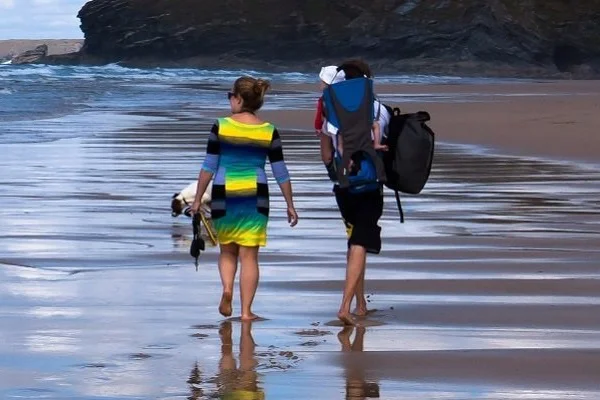 Kaufberatung Kindertrage Outdoor Imagebild - zwei Personen laufen am Strand in flachem Wasser, eine Person trägt eine Kindertrage auf dem Rücken