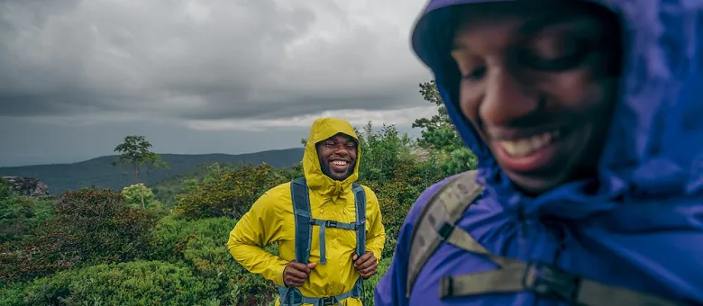 Outdoor-Imagebild - zwei Personen sind in den Bergen bei nass-grauem Wetter - sie sind mit Regenjacken gekleidet und lachen.