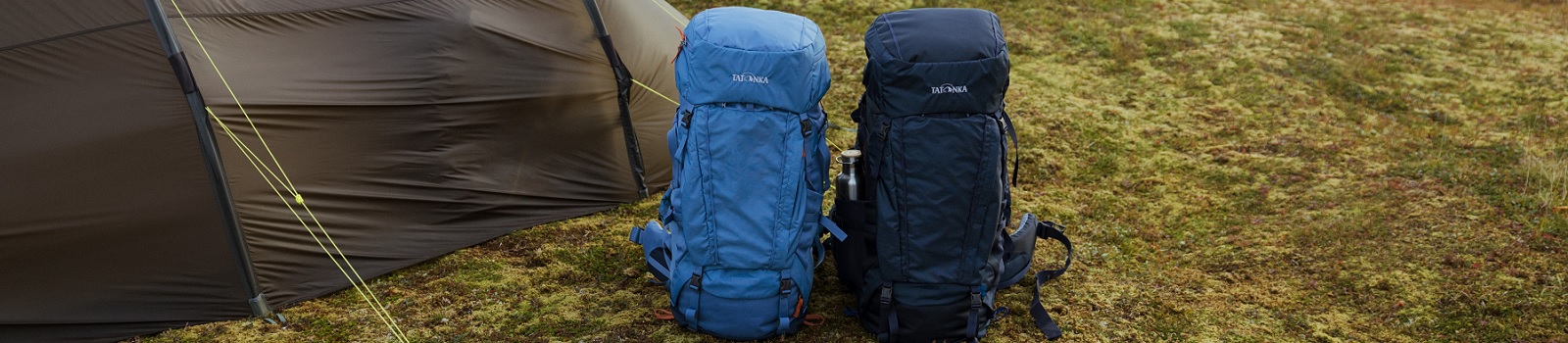 zwei blaue Tatonka Yukon Rucksäcke stehen nebeneinander auf einem Boden neben einem Zelt