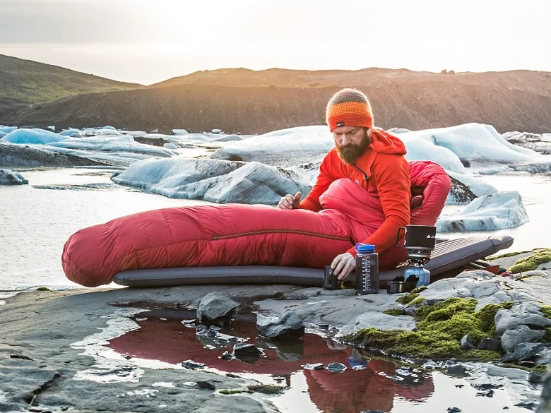 Kaufberatung Schlafsacke Outdoor Imagebild - Person im freien auf einer Isomatte in einem Schlafsack - in der Umgebung ist eine kalte Eislandschaft bzw. Felslandschaft
