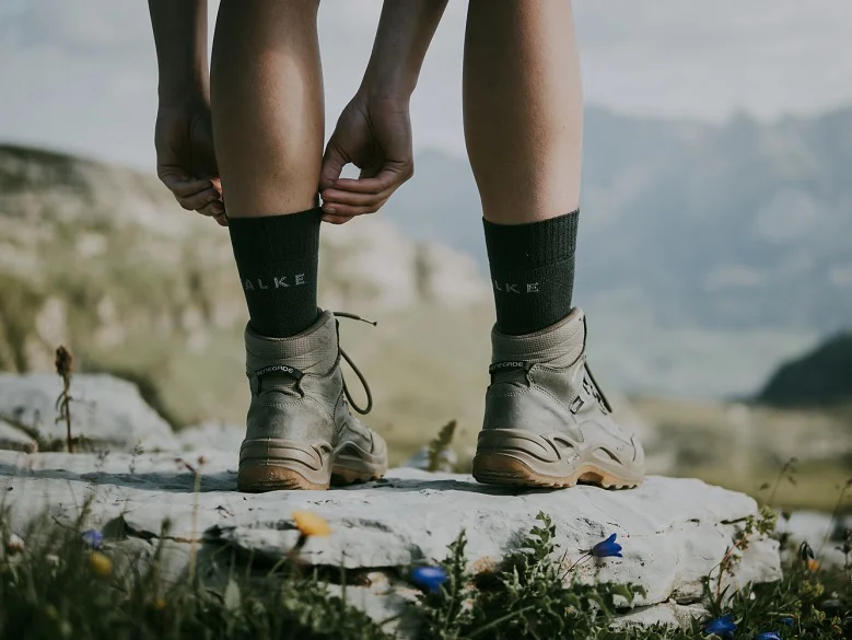 Outdoor Imagebild - Person steht auf einem Felsen in Wanderschuhen und Wandersocken. Man sieht nur die Unterschenkel und Füße bzw. Schuhe.
