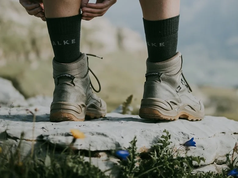 Outdoor Imagebild - Person steht auf einem Felsen in Wanderschuhen und Wandersocken. Man sieht nur die Unterschenkel und Füße bzw. Schuhe.