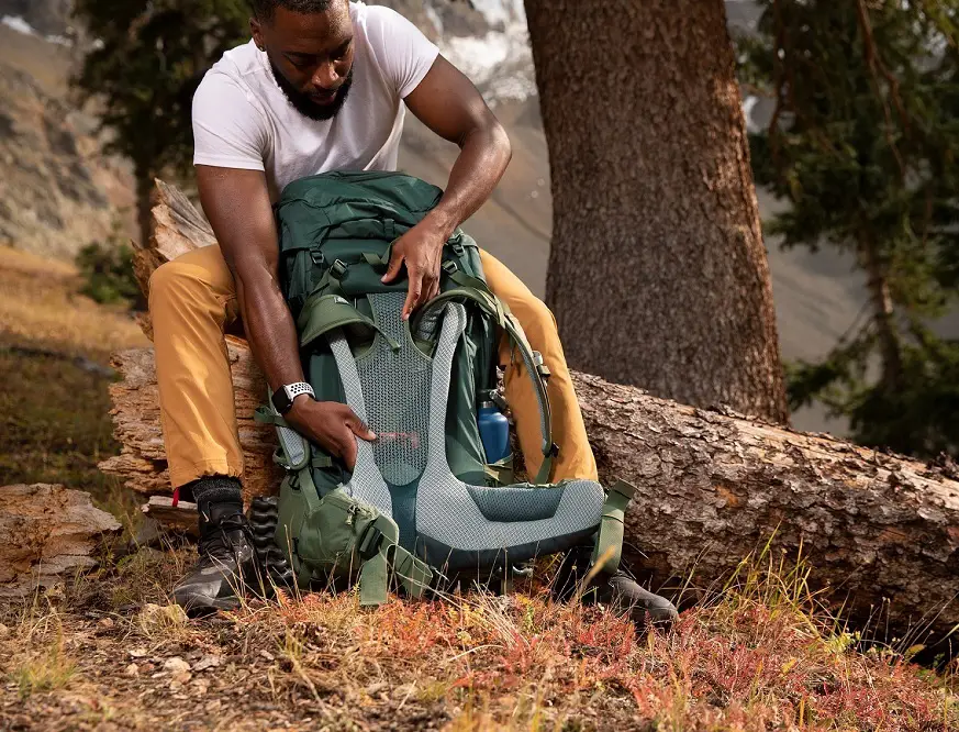 deuter Futura Rucksack in Aktion - Person sitzt in einem Wald auf einem Baumstamm und verstellt das Tragesystem eines grünen deuter Futura